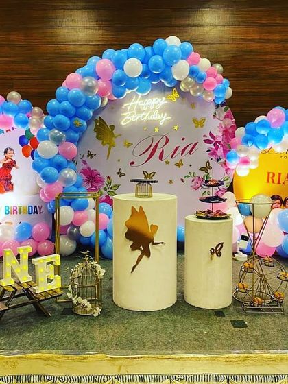 A beautiful fairy-themed birthday with butterfly accents. The stage features two balloon arrangements in pink and blue, a personalized backdrop, and elegant cake plinths.