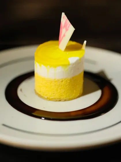 A beautifully plated Mango and White Chocolate Mousse cake. The vibrant yellow of the mango contrasts with the white chocolate layer, creating a visually appealing and delicious dessert.