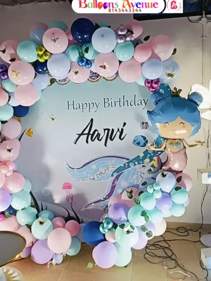 A detailed shot of the mermaid-themed circular backdrop, surrounded by a pastel balloon garland and a large light-up number '1'.