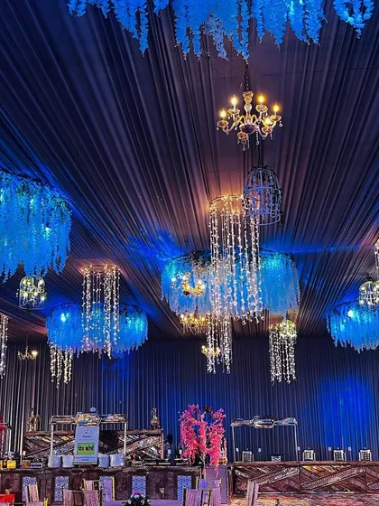 A look at an elaborate ceiling treatment for a dining area. The dark blue draping is accented with hanging floral chandeliers and crystal strings, creating a starry night effect.