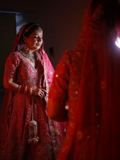 A quiet moment of reflection for the bride before her ceremony. The soft lighting highlights the beautiful details of her red lehenga and the subtle glow of her makeup.
