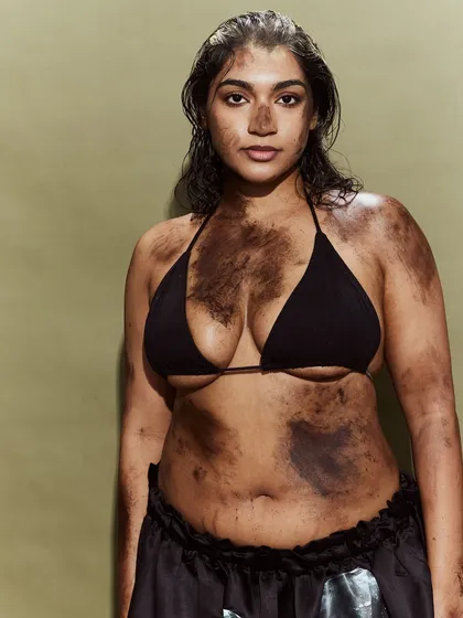 A bold and unconventional runway look, pairing a simple bikini top with a deconstructed skirt and raw, textured makeup.