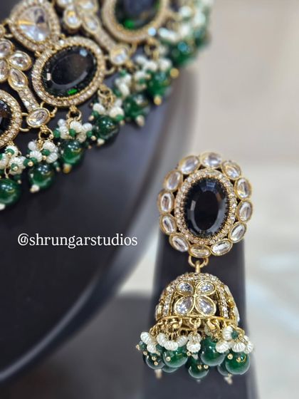 The matching jhumkas are equally striking, with a central black stone surrounded by ADs.