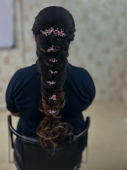 A long, thick fishtail braid decorated with delicate pink floral pins, a beautiful style for any festive occasion.