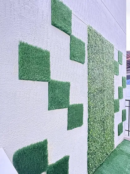 A side view of the geometric square tile installation. This angle highlights the 3D texture of the artificial grass tiles against the flat wall, showcasing the design's depth.