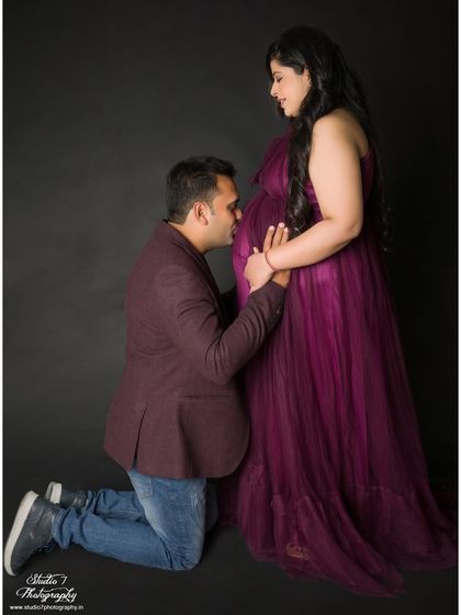 A touching studio pose where the dad-to-be kneels to kiss the baby bump. The dark background eliminates distractions, making the moment even more powerful.