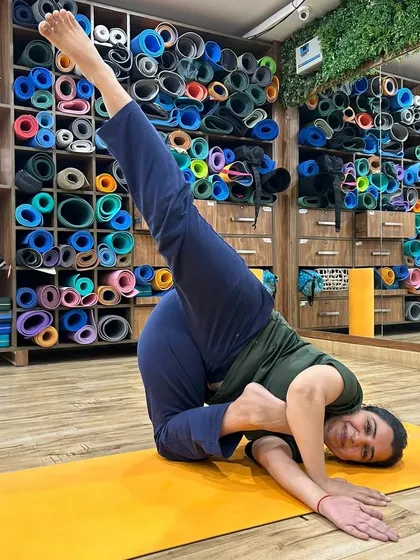 A student smiles as she holds a challenging twisted pose. The colorful background of yoga mats highlights the vibrant energy of our well-equipped studio.
