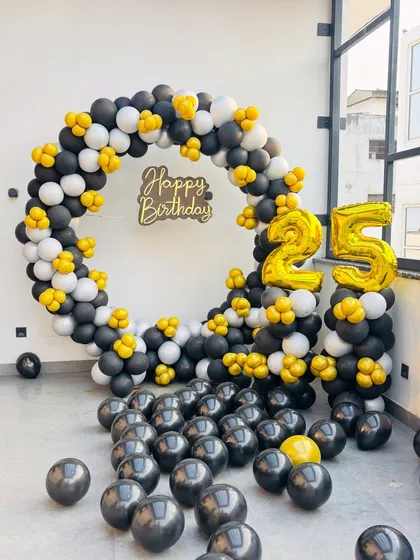 A bold and modern 25th birthday setup. The circular balloon arch in black, white, and yellow with matching marquee numbers creates a striking photo backdrop.
