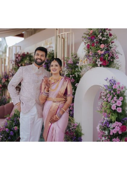 A happy couple posing in front of their engagement backdrop. The combination of modern white arches and lush, colorful floral arrangements creates a stunning visual for their memorable photos.