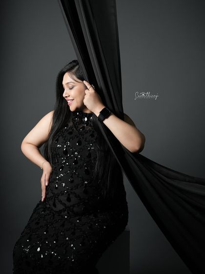 A glamorous portrait of a mother-to-be in a black sequined gown, playing with a flowing black fabric. The movement and texture add a dynamic and artistic element to the shot.