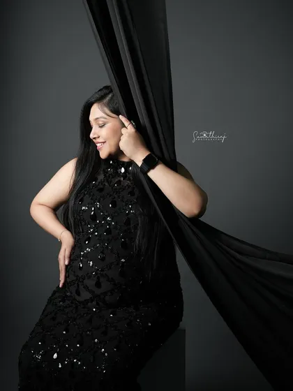 A glamorous portrait of a mother-to-be in a black sequined gown, playing with a flowing black fabric. The movement and texture add a dynamic and artistic element to the shot.