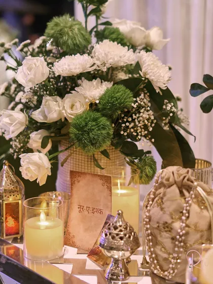 A close-up of a table centerpiece, featuring a 'Noor-e-Ishq' card, a traditional lantern, and a pearl-adorned pouch, capturing the essence of the Sufi theme.