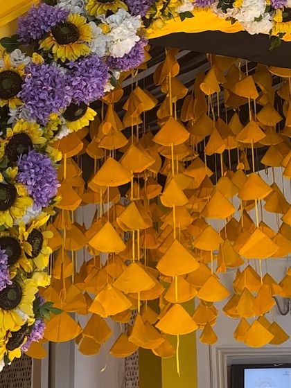 A unique and vibrant detail for a Haldi entrance. This close up shows the hanging yellow fabric cones and the lush arch of sunflowers and purple flowers that created a memorable entryway.