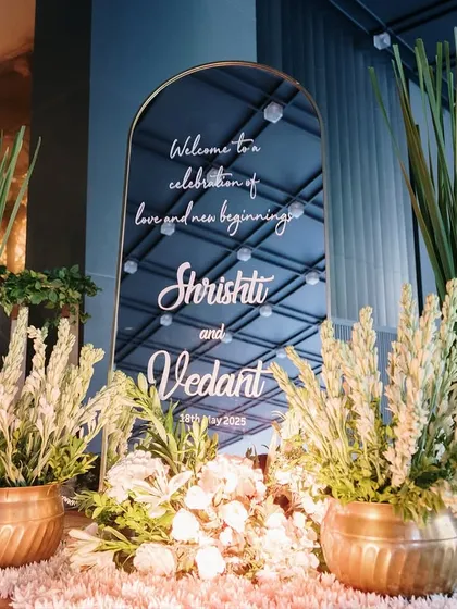 A personalized welcome mirror for an elegant white wedding, flanked by tall grasses and white tuberose in copper pots. This entrance sets a sophisticated and welcoming tone for the guests.