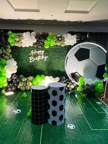 A dream setup for a young football fan. We transformed the space with an artificial grass floor, a giant football backdrop, a 'Happy Birthday' neon sign, and balloon decorations in the team's colors.