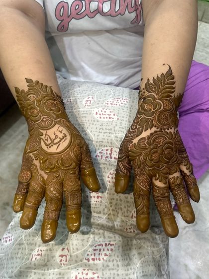 A full view of the personalized mehendi with the name in Arabic script. The design is asymmetrical, with one hand featuring the custom element.