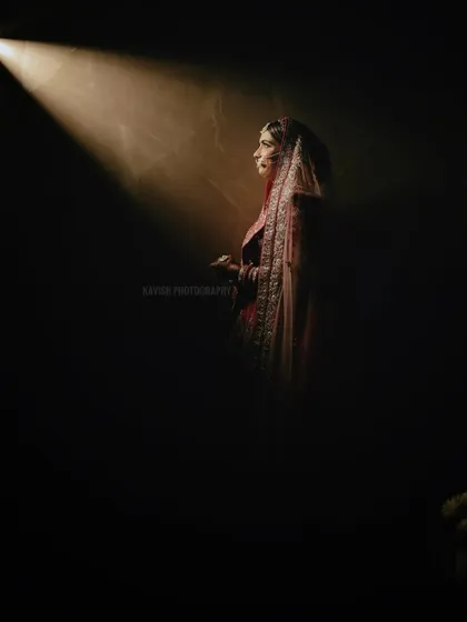 A solitary bridal portrait using dramatic spotlighting. The bride is captured in profile, creating a sense of anticipation and quiet beauty before the ceremony.