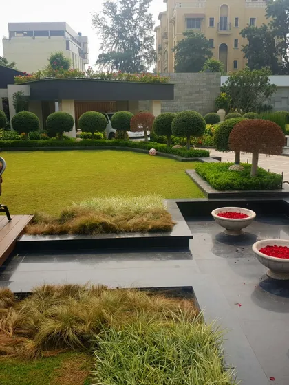This garden design shows a seamless transition from the home's interior to the outdoor space. A wooden deck and water feature with floating flower bowls lead to a lush lawn with carefully shaped trees and shrubs, exemplifying our holistic approach.