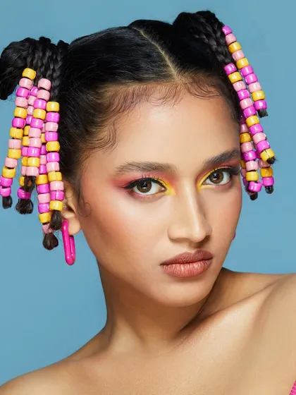 A playful and colorful look with pink and yellow eyeshadow and beaded braids, perfect for a fun, youthful vibe.