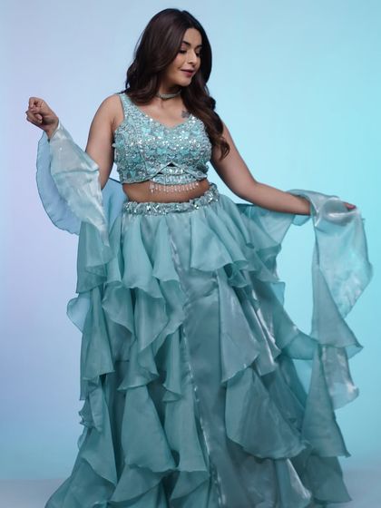 A full-length view of the sky-blue ruffled lehenga. The layers of organza create a beautiful, flowing silhouette that's made for movement.