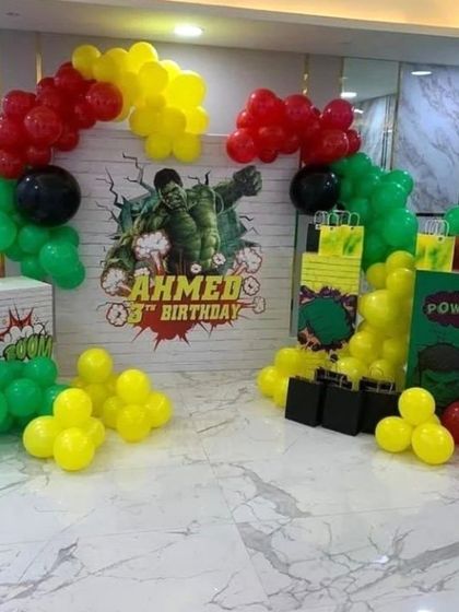 A powerful Hulk themed birthday party setup. The decoration uses green, yellow, and red balloons to match the comic book hero's colors, framing a dynamic backdrop.