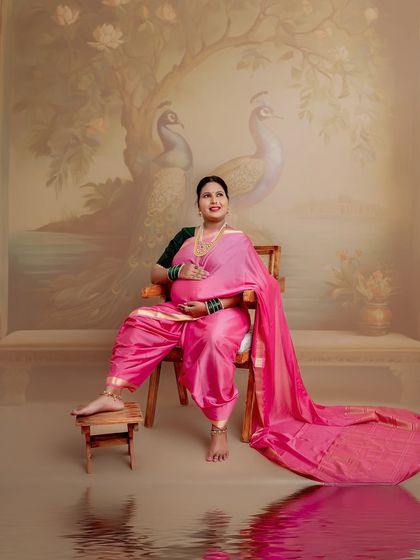 Seated on a traditional wooden chair with a painted peacock backdrop, this portrait is a celebration of Indian artistry and the grace of motherhood. The flowing saree adds a touch of royalty.