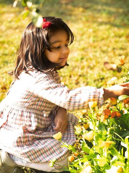 A two-year-old girl curiously touching the flowers in a garden. I love capturing these small moments of discovery during our outdoor photoshoots.