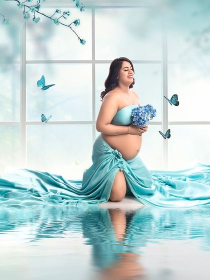 A dreamy and serene portrait with a water reflection. The client is surrounded by soft blue fabric and floating butterflies, creating a magical and peaceful atmosphere.