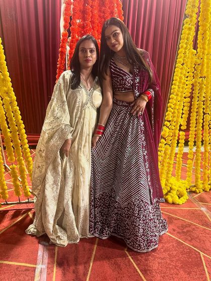 A photo of me with a client, who is wearing a maroon chevron lehenga. She is standing next to another client in one of my custom ivory gowns.