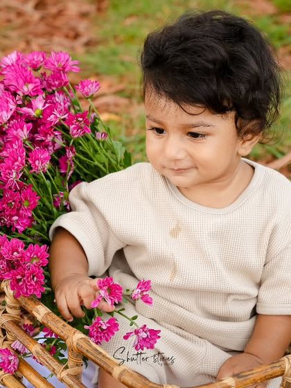 An outdoor sitter session with a baby boy in a basket, holding a bouquet of bright pink flowers.