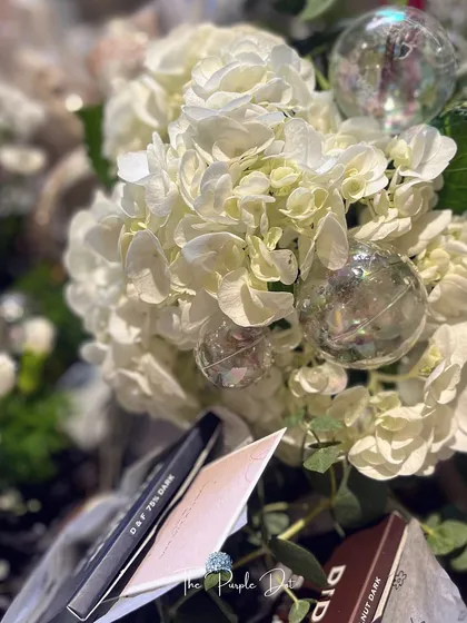 A close-up of the details in a founder's gift. White hydrangeas, delicate bubble-like ornaments, and artisanal dark chocolate come together to celebrate a personal milestone with sophistication.