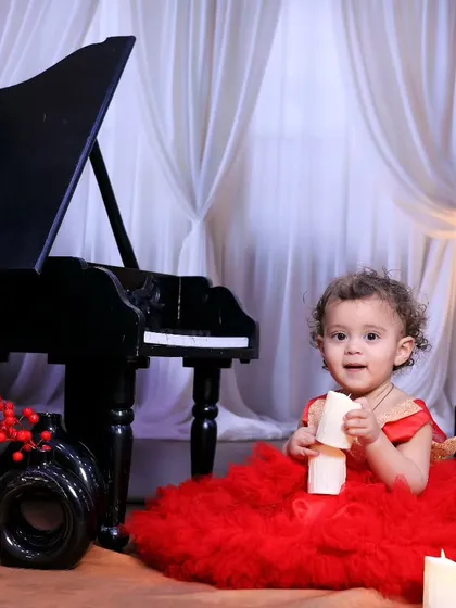 A classic and elegant portrait of a little girl in a beautiful red dress, sitting by our miniature grand piano.