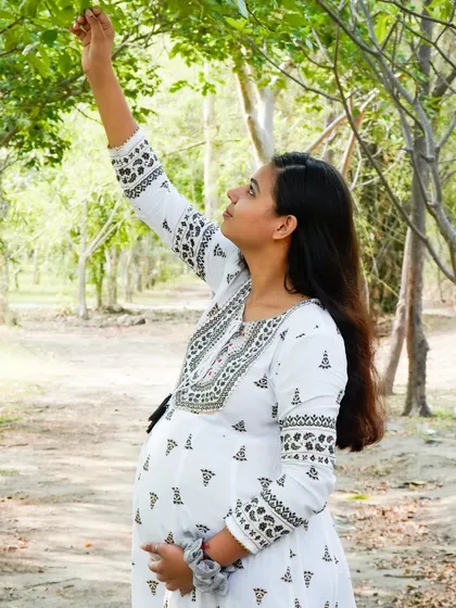 A candid photo of an expecting mother reaching for a branch in a park. We encourage natural movements to create authentic and beautiful images.