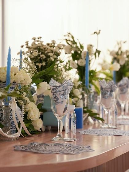 A long dining table set with blue candles and arrangements of white flowers and baby's breath.