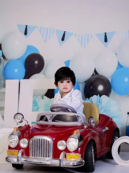 A one-year-old boy takes the wheel of a red toy car in our "Little Man" themed shoot, complete with a tie-themed banner and balloons.