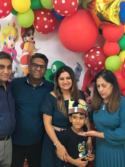 The whole family is here to celebrate! Grandparents, parents, and the birthday boy, Krishav, pose for a photo at his Super Mario party.