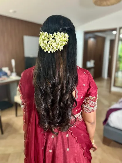 A half-up hairstyle with beautiful curls, adorned with a string of fresh jasmine (gajra) for a traditional yet modern feel.