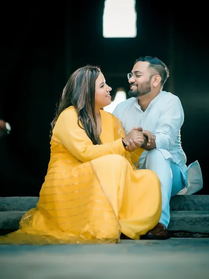 A casual and happy pre-wedding moment. The couple, dressed in yellow and white, shares a laugh while sitting on stone steps, creating a relaxed and natural portrait.