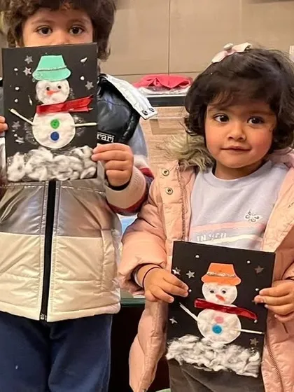 Two of our youngest artists hold up their finished snowman cards. These mixed-media projects are great for teaching toddlers about different textures and materials.