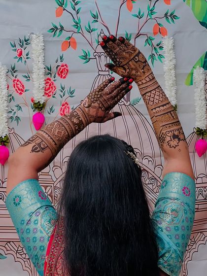 A back view of a bride showing off her full-arm mehendi, with detailed patterns extending up to her elbows.