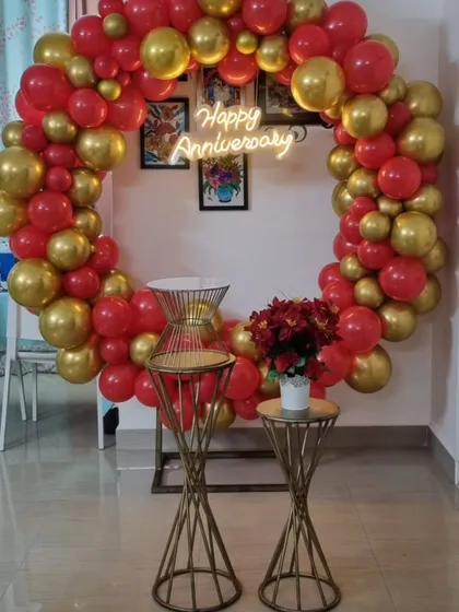 A vibrant red and gold balloon ring setup for an anniversary party at home. The 'Happy Anniversary' neon sign adds a modern touch to this celebratory decoration.