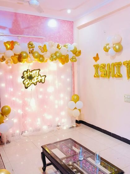 An elegant and simple living room decoration. I used a white and gold balloon garland, a "Happy Birthday" neon sign against a fairy light curtain, and foil letters for the name "ISHITA".