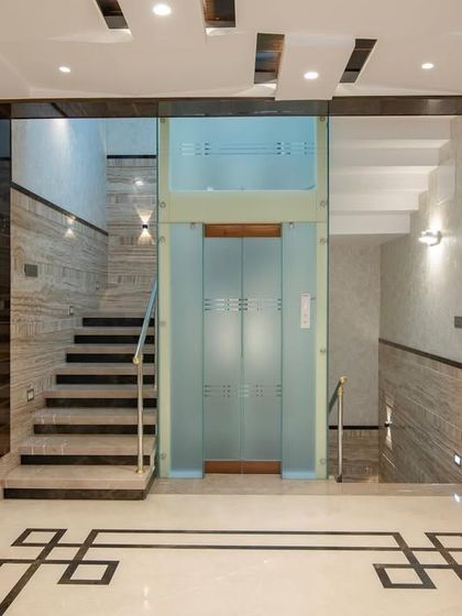 The lift and staircase area in the "Chic Adobe," showcasing travertine wall cladding and a geometric floor pattern.