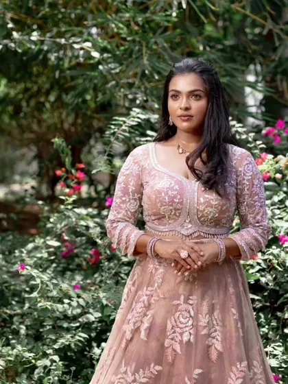 A model posing in a beautiful pink lehenga, showing off a subtle and elegant makeup look.