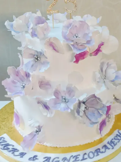 A beautiful two-tiered anniversary cake decorated with hand-painted wafer paper flowers in shades of purple and white.