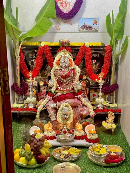 The soft glow of the lamps illuminates the pink silk saree on the Goddess, creating an atmosphere of divine peace.