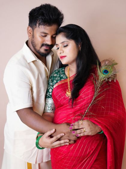An intimate portrait of a couple in traditional attire. The mother-to-be holds a peacock feather, adding a touch of divine symbolism.