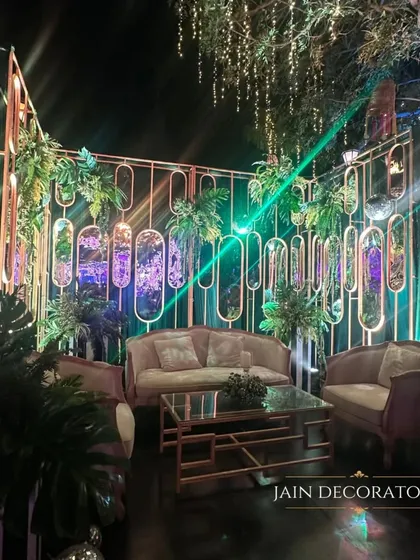 A chic lounge area for guests to mingle. The modern backdrop with mirrored panels and hanging plants creates a sophisticated and stylish atmosphere for a cocktail evening.