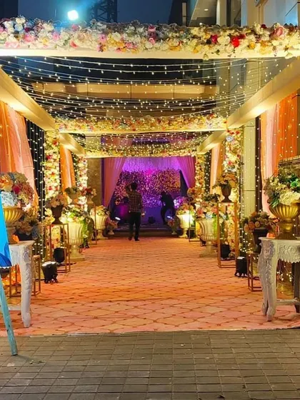 A grand and colorful floral entrance for an indoor reception. The arch is covered in a vibrant mix of flowers, and the path is lined with elegant golden vases, creating a lavish welcome.