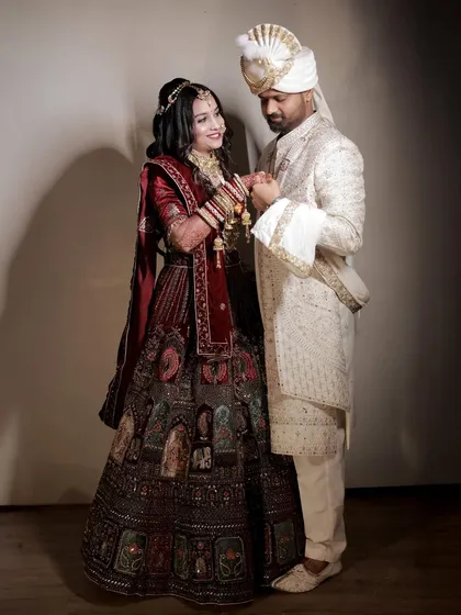 A classic, full-length portrait of the couple holding hands and sharing a gentle look. The bride's magnificent lehenga and the groom's elegant sherwani are beautifully displayed.